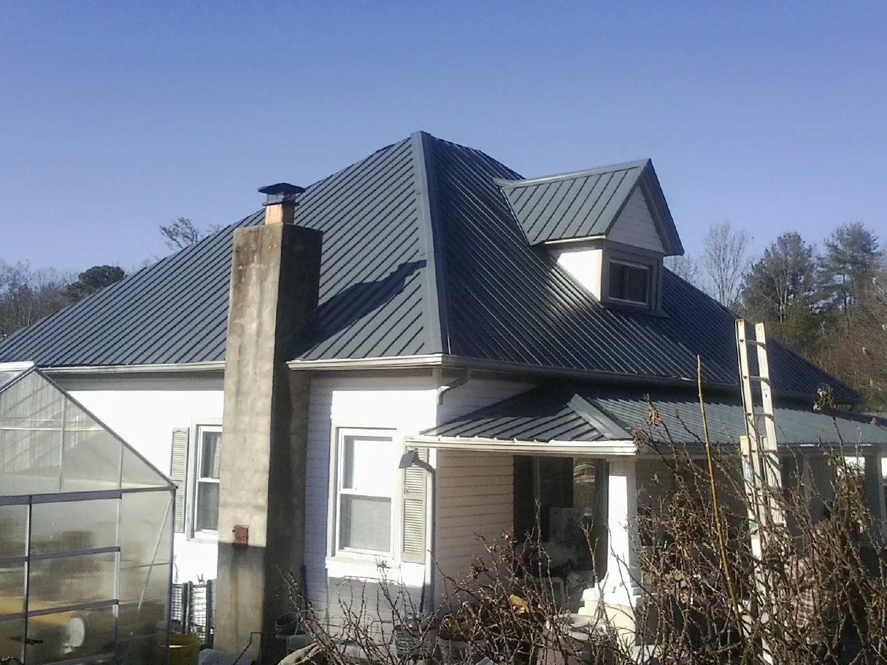 Dark blue standing seam metal roof on a white farmhouse with dormer — Slate & Tile Roof Repair by Roofing Brothers in Norlina