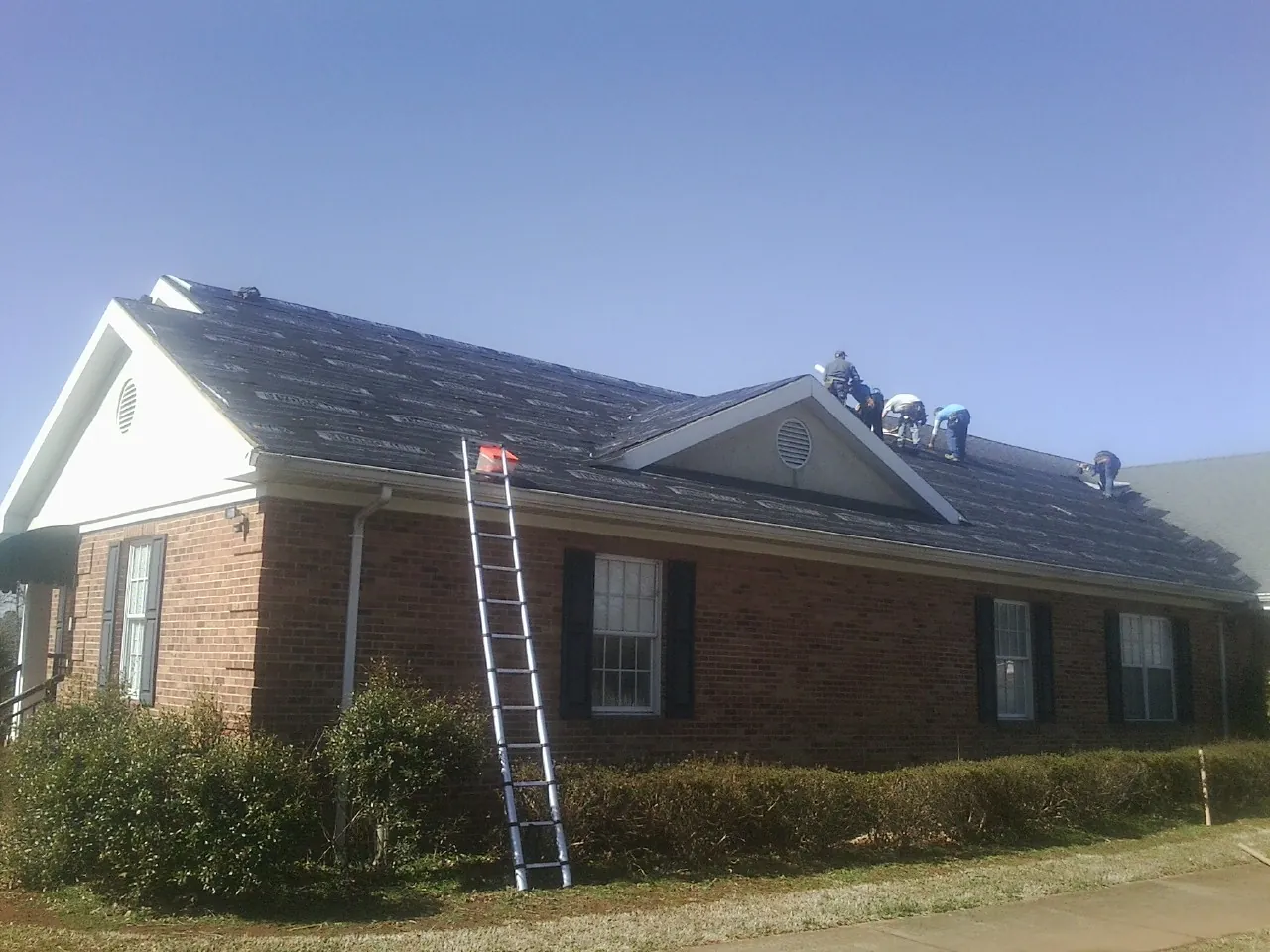 Crew tearing shingles off a brick ranch roof with a ladder set — Emergency Roof Repair work by our crew in Norlina