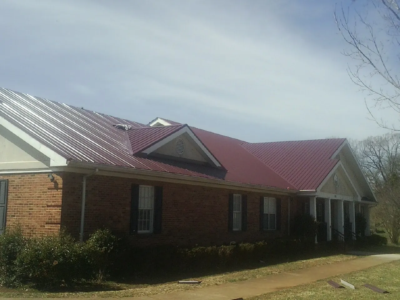 Red metal roof with gabled entries on a long brick building, from a Hail Damage Roof Repair job in Norlina