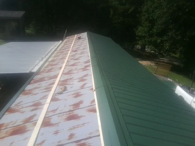 Old rusted panels beside newly installed green metal roofing — Wind Damage Roof Repair by Roofing Brothers in Norlina