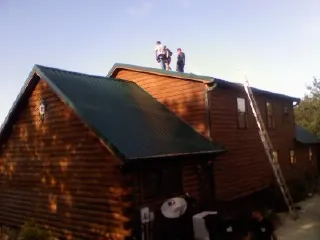 Crew on the ridge of a green metal roof on a two story log home in Norlina
