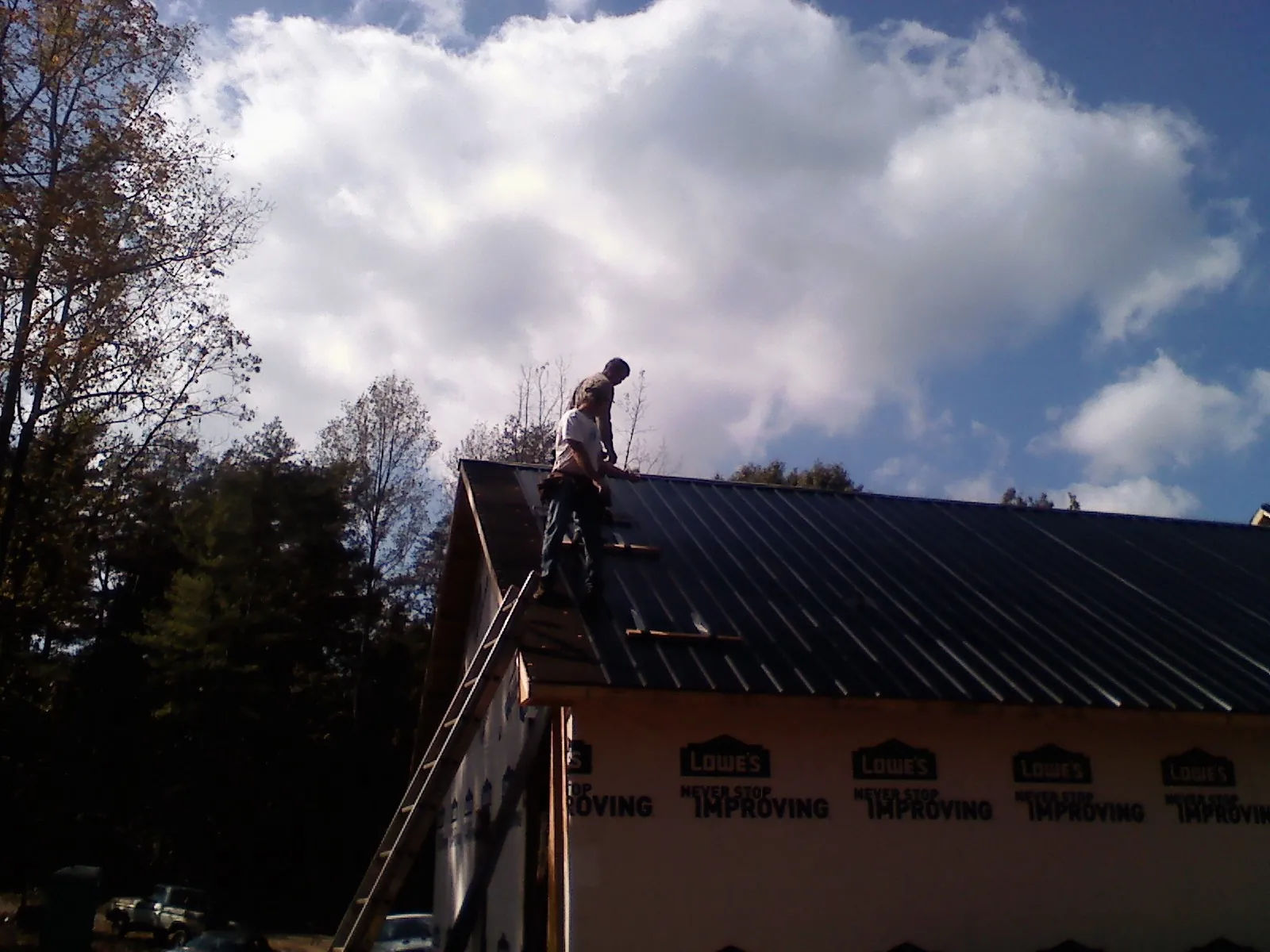 Roofer fastening dark metal panels high against a cloudy sky, from a Roof Inspection job in Norlina