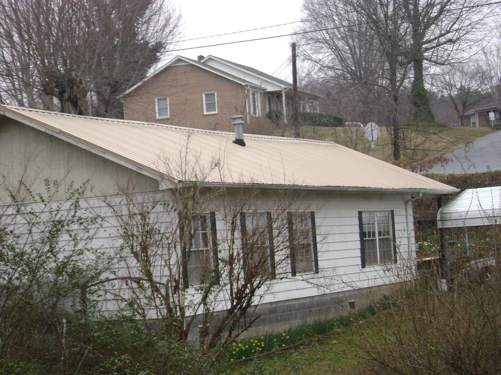 Tan metal roof on a white sided house set into a hillside — Commercial Roofing by Roofing Brothers in Norlina