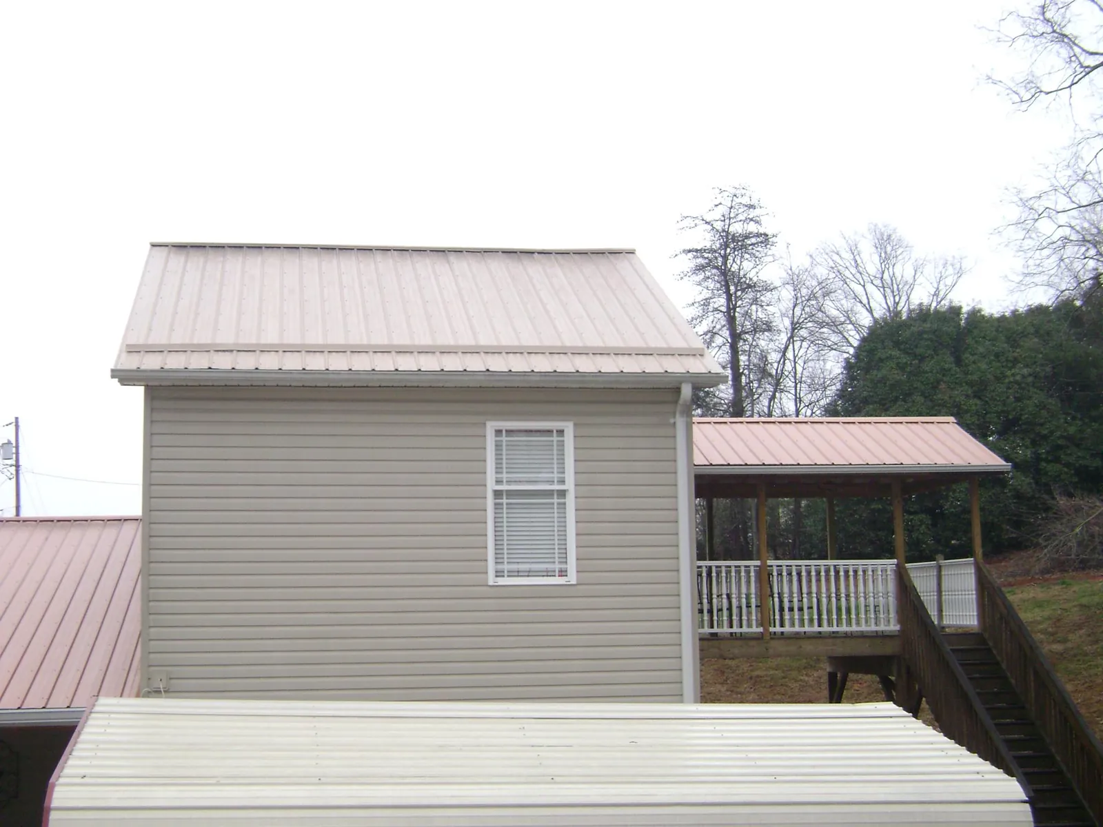 Tan metal roofs on a two story addition and attached porch, from a Roof Replacement job in Norlina